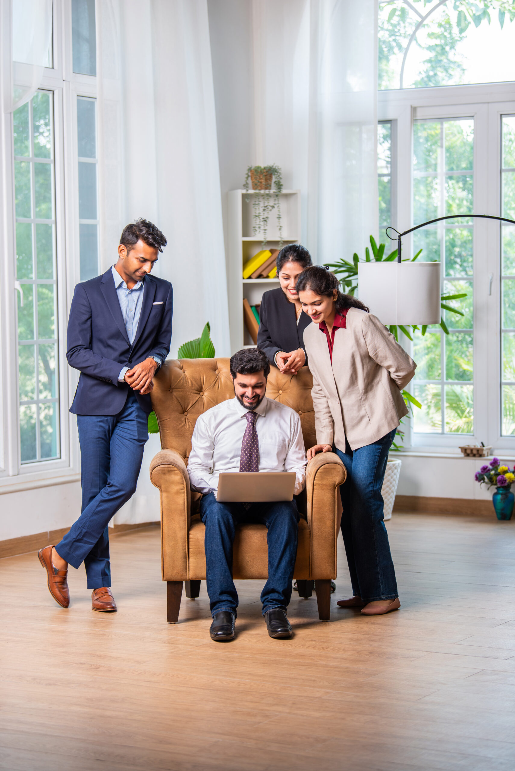 group of indian asian young business people men and woman in group sitting around wing chair using laptop in office